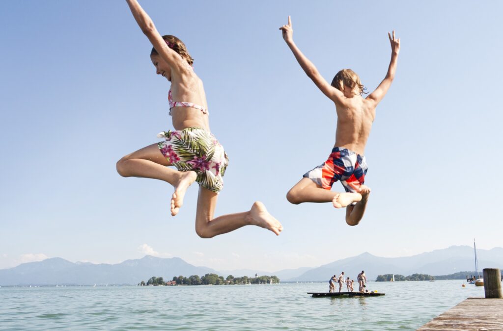 Zwei Kinder hüpfen in einen der schönsten Badeseen Bayerns, den Chiemsee
