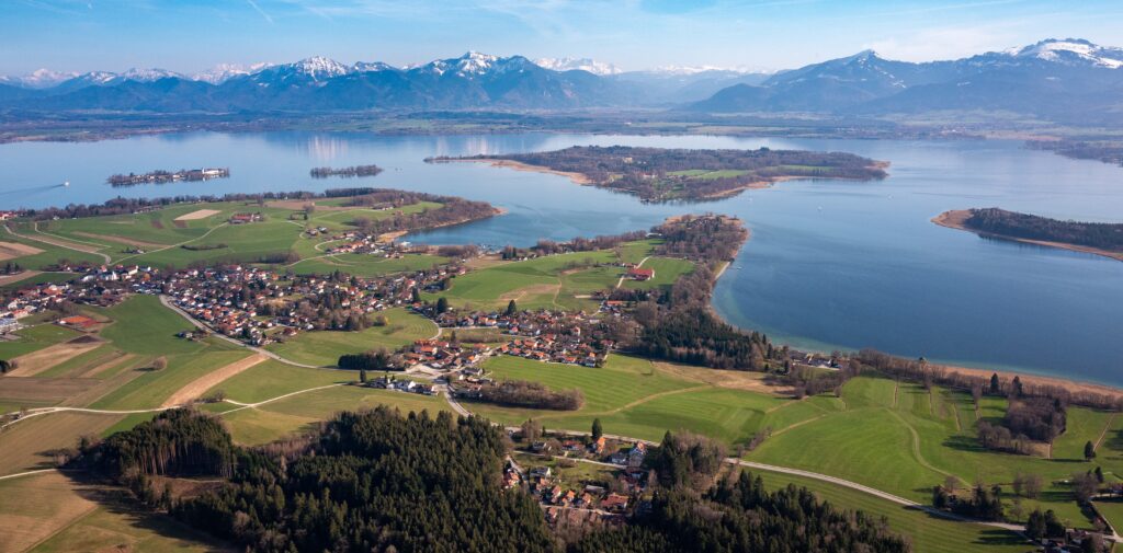 Geheimtipp für einen schönen See in Bayern: Der Chiemsee von oben mit schneebedecktem Alpenpanorama im Hintergrund
