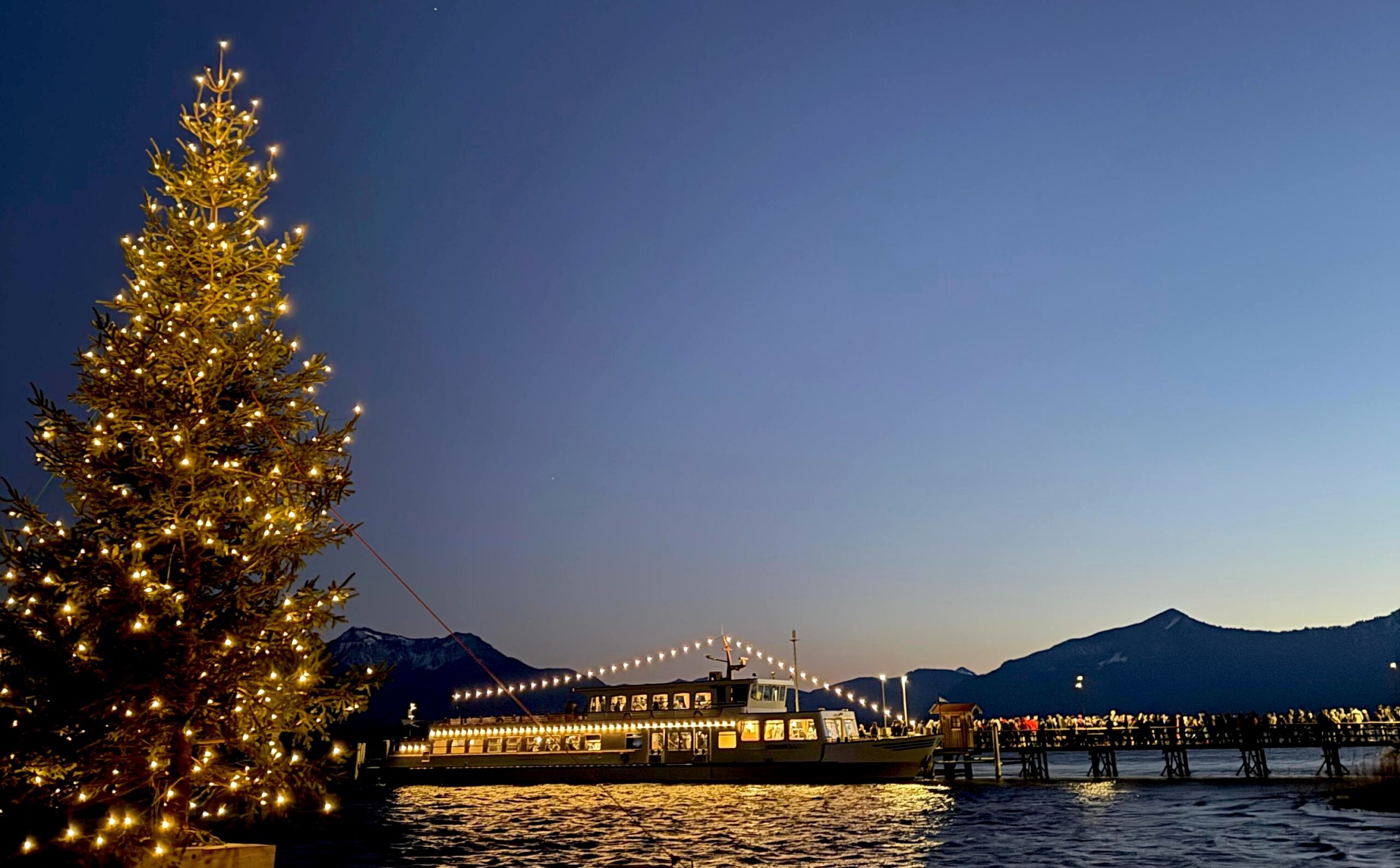 Weihnachtsmarkt am Chiemsee bei Abendstimmung mit Christbaum und Lichterketten am Schiff