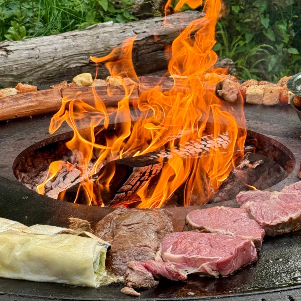 Auf dem Kugelblitzgrill liegt Fleisch während in der Mitte des Grills das Feuer lodert.