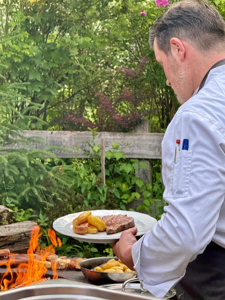 Der Koch des Raitner Wirts belegt, nach dem Grillen, die Teller mit Fleisch und Kartoffeln.