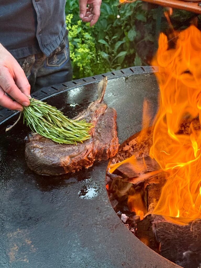 Der Koch des Rainter Wirts streicht mit einem Rosmarienzweig das Fleisch ein.