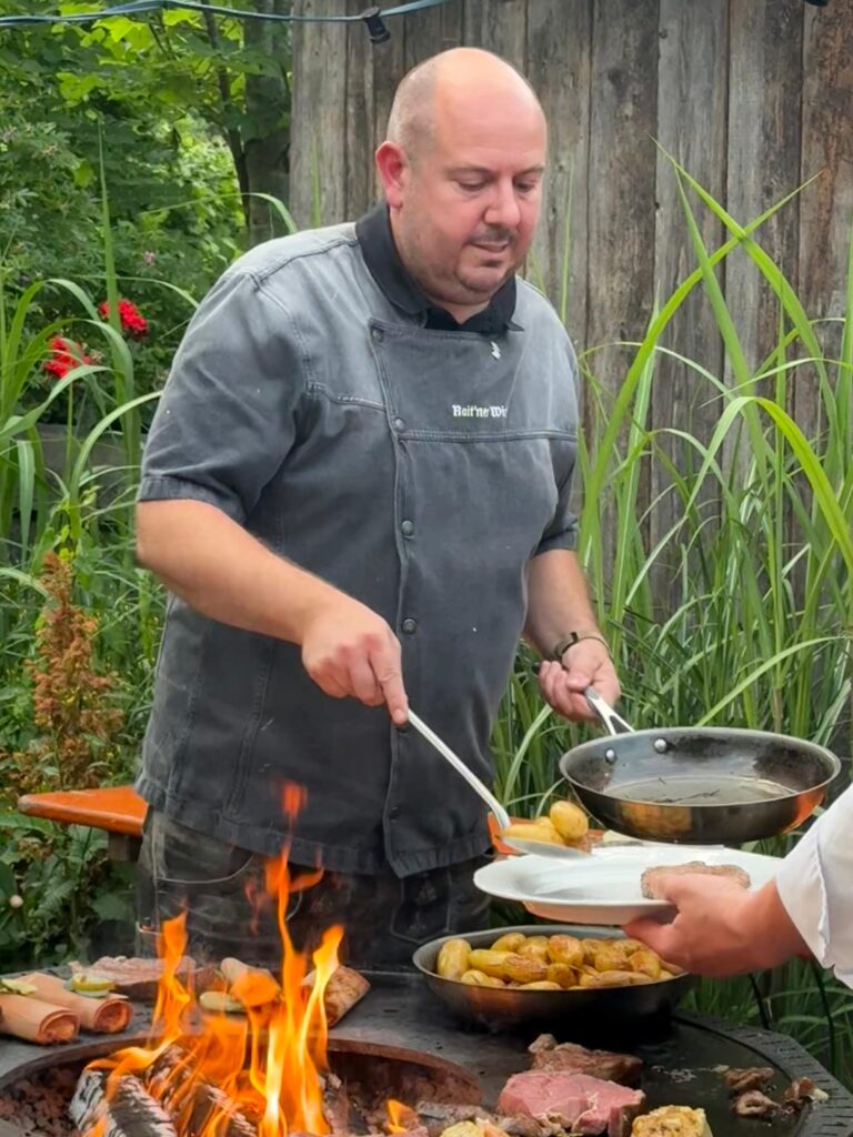 Der Wirt gibt den Gästen das Essen vom Grill auf dem Teller.